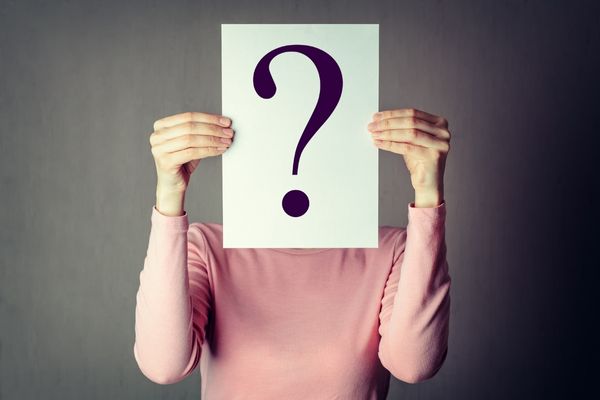 Woman holding up question mark to obscure her identity